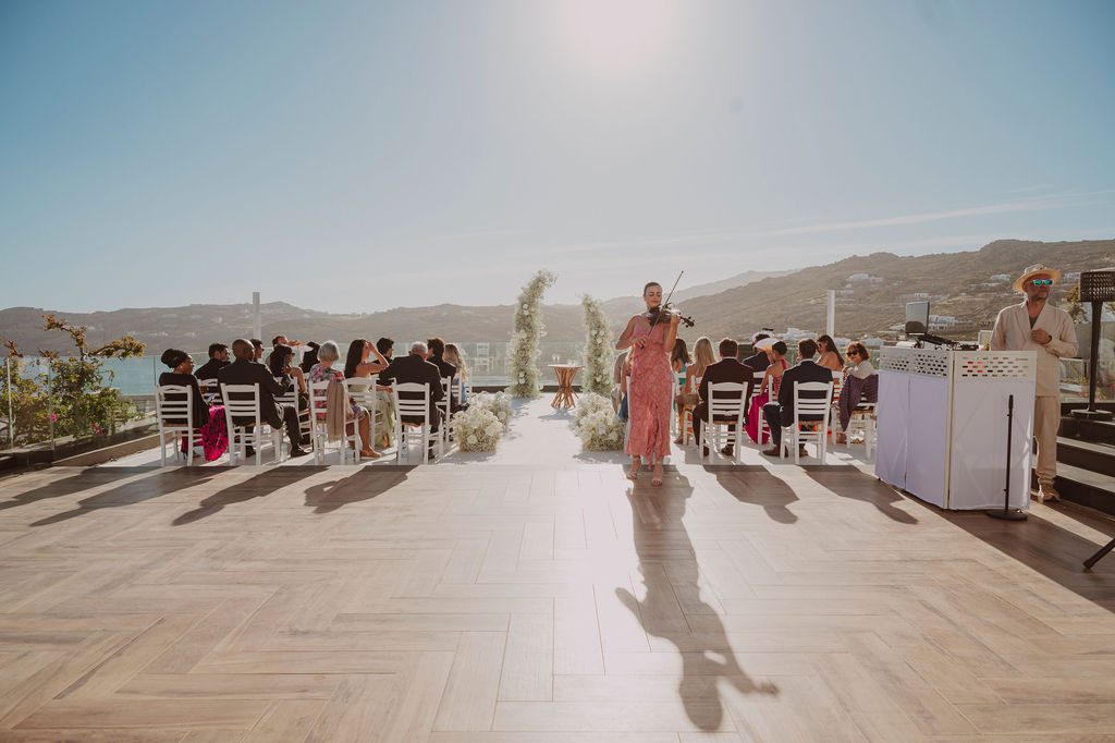 Mykonos destination wedding ceremony setup at Royal Myconian, Elia – violin and DJ booth