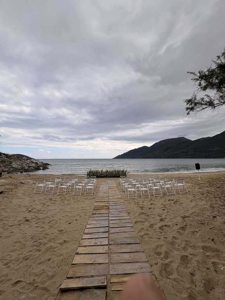 Wedding ceremony setup on Skoutari beach, Mani, with floral arch and white chairs facing the sea